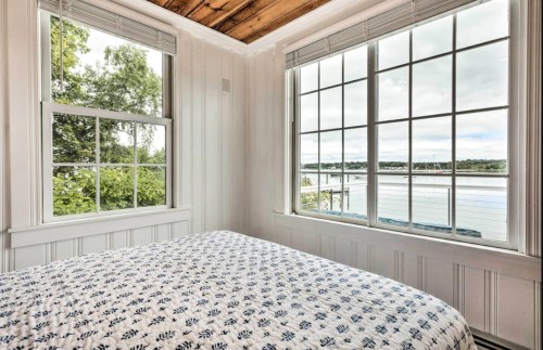 Cozy bedroom with a patterned bedspread and large windows overlooking a serene waterfront view.
