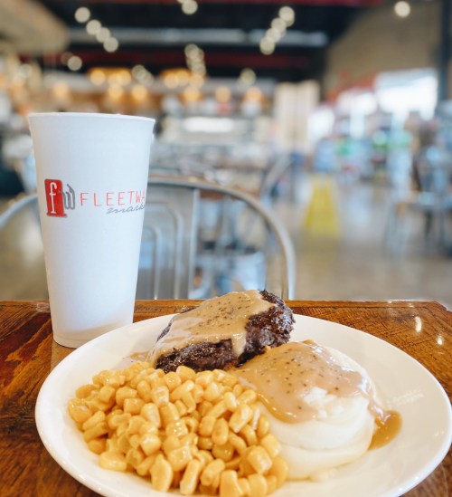 A plate of meatloaf with gravy, mashed potatoes, and corn, alongside a large drink in a casual dining setting.