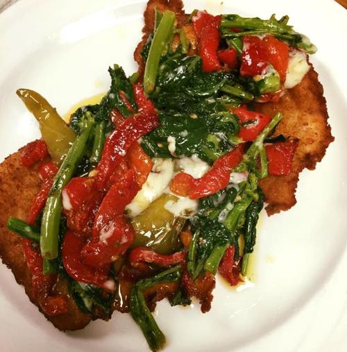 A crispy fried dish topped with sautéed greens, red peppers, and melted cheese on a white plate.