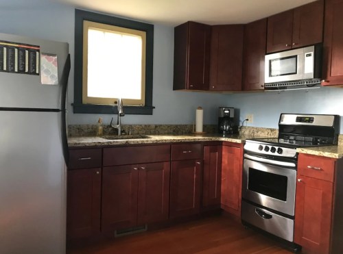 A modern kitchen with dark wood cabinets, stainless steel appliances, and a granite countertop. Natural light from a window.