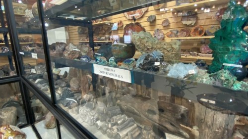 Display case filled with various Arizona copper minerals and colorful gemstones in a museum setting.