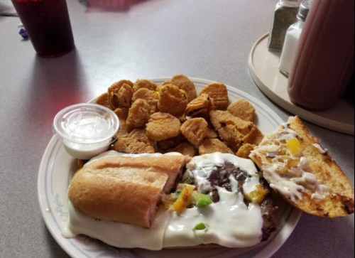 A plate with a sandwich topped with cheese and peppers, alongside a serving of chicken nuggets and dipping sauce.
