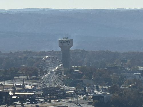 A distant view of a water tower and a ferris wheel, surrounded by rolling hills and a clear sky.
