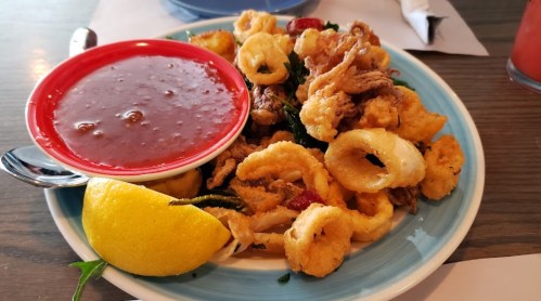 A plate of fried calamari with a side of marinara sauce and a lemon wedge.