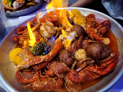 A seafood platter with crawfish, shrimp, corn, and potatoes, topped with flames and spices.