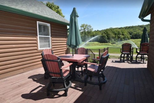A patio with a wooden table and chairs, surrounded by greenery and featuring a large umbrella.