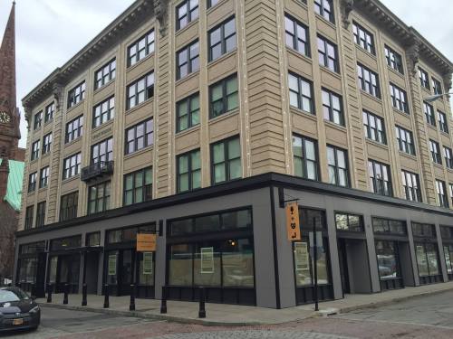 Historic building with large windows, corner location, and modern storefronts, set against a cloudy sky.