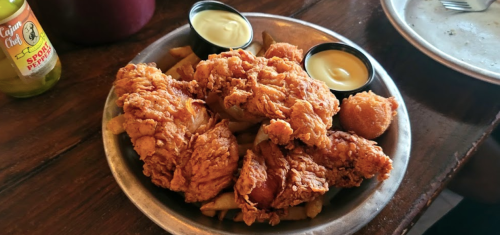 A plate of crispy fried chicken with fries and two dipping sauces on the side.