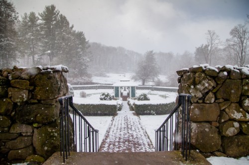 A snowy landscape with stone steps leading to a garden path, surrounded by trees and a misty atmosphere.