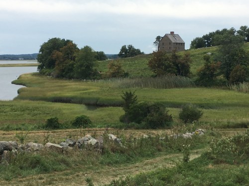 A serene landscape featuring a house on a hill, surrounded by lush greenery and a calm waterway.