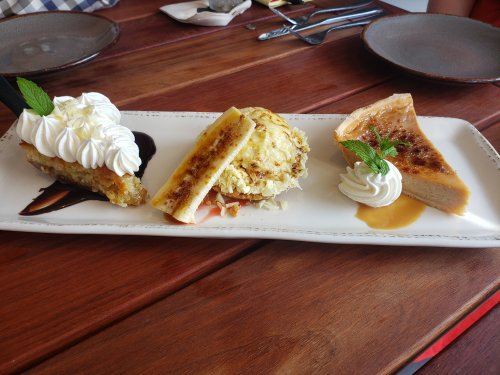 A dessert platter featuring three treats: a slice of cake with whipped cream, a baked banana, and a creamy tart.