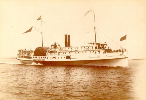 A historic steamboat named "Portland" sails on water, adorned with flags and carrying passengers on board.