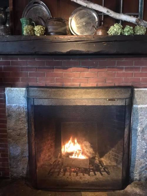 A cozy fireplace with a fire burning, surrounded by a brick hearth and decorative items on the mantel.