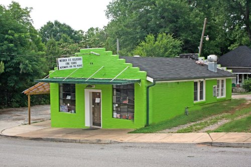 A bright green building with a sign, surrounded by trees and a gravel path, showcasing a unique architectural style.
