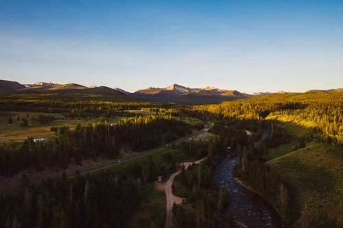 Aerial view of a lush valley with a winding river, mountains in the background, and a clear blue sky at sunset.