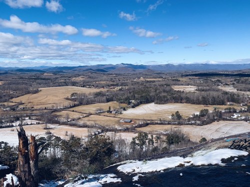 A panoramic view of rolling hills and fields under a blue sky with scattered clouds, showcasing a rural landscape.
