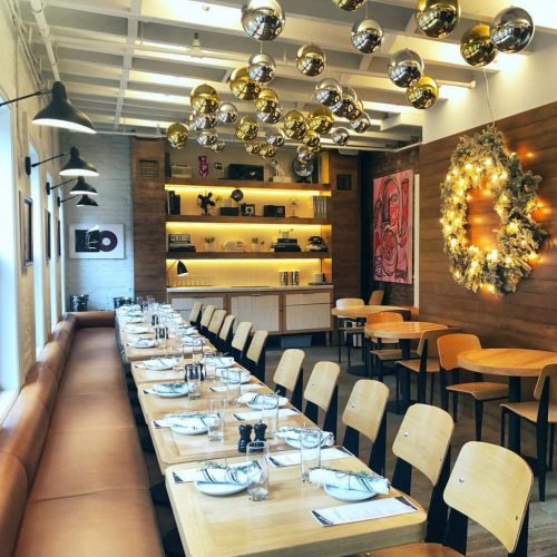 A modern restaurant interior with a long table set for dining, decorated with festive ornaments and a wreath.
