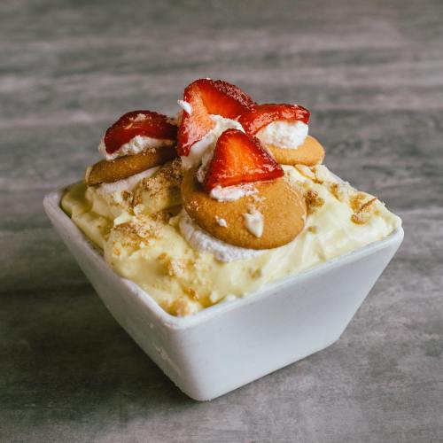 A dessert bowl filled with creamy pudding, topped with sliced strawberries, whipped cream, and vanilla wafers.