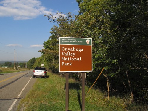 Sign for Cuyahoga Valley National Park along a roadside, with trees and a vehicle in the background.
