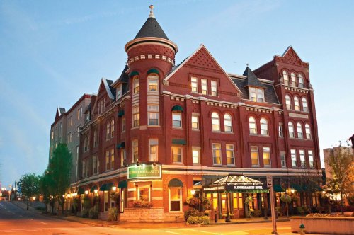 Historic red brick hotel with a turret, featuring green awnings and a welcoming entrance, set against a clear blue sky.