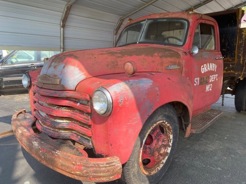 A vintage red truck with rust and wear, marked "Granby Street Dept. W22," parked under a shelter.