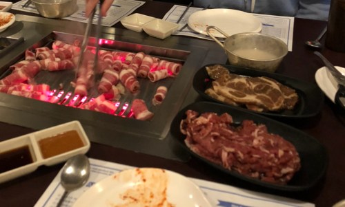 Grilled meat on a tabletop barbecue with various raw meats and dipping sauces nearby.