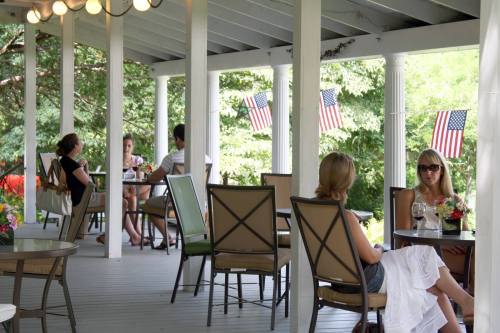 A porch with people sitting at tables, enjoying drinks, and American flags hanging in the background.