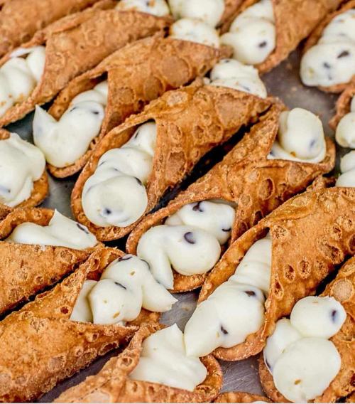 A close-up of crispy cannoli shells filled with creamy ricotta and chocolate chip filling.