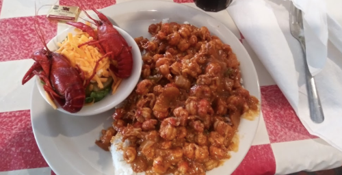 A plate of crawfish étouffée served with rice, alongside a side salad topped with cheese and a crawfish.