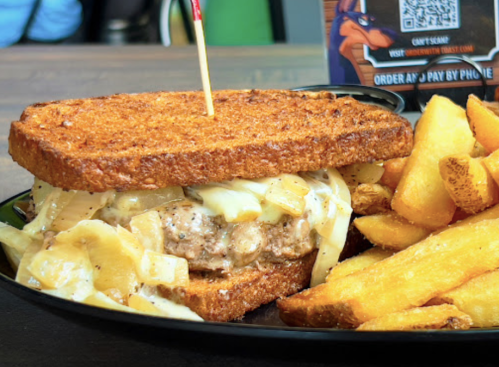 A hearty sandwich with grilled chicken, onions, and cheese on toasted bread, served with golden fries on the side.