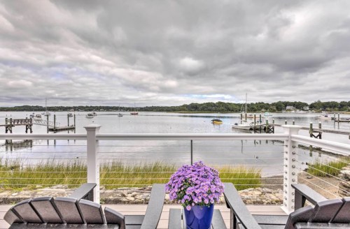 A serene waterfront view with a flower pot in the foreground, boats on the water, and cloudy skies above.