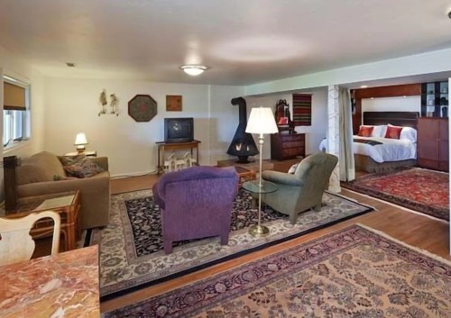 Cozy living space with a sofa, armchairs, lamp, and a bedroom area featuring a bed and decorative rugs.