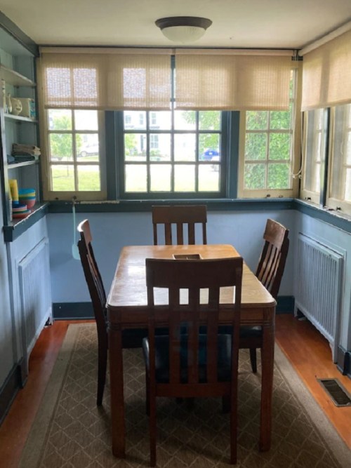 A cozy dining area with a wooden table and four chairs, featuring large windows and natural light.
