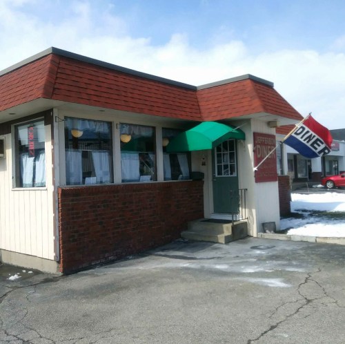 A small diner with a red roof, green awning, and a "Diner" sign, set against a cloudy sky.