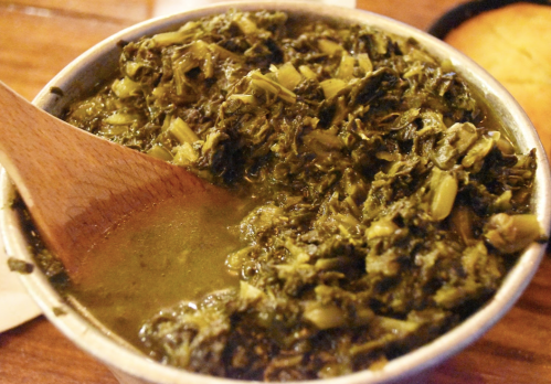 A bowl of green leafy stew with a wooden spoon, showcasing a rich, textured mixture.