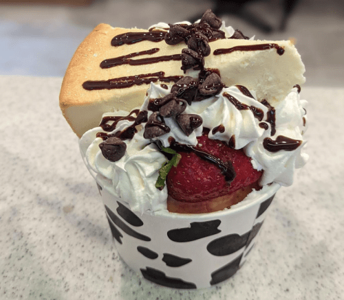 A dessert cup filled with whipped cream, strawberries, chocolate chips, and a slice of cake drizzled with chocolate sauce.
