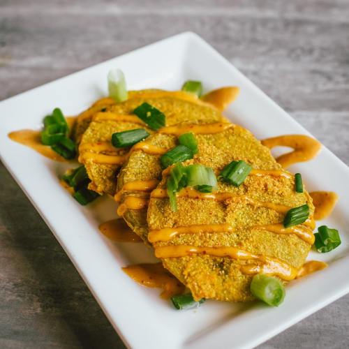 Three golden corn tortillas topped with green onions and drizzled with a creamy sauce, served on a white plate.