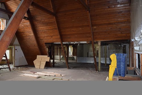 Interior of a partially renovated space with wooden beams, exposed walls, and construction materials scattered on the floor.