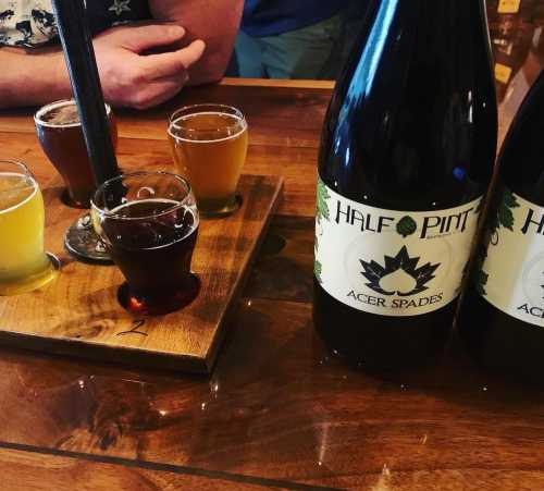 A wooden table with a flight of small beer glasses and two large bottles labeled "Half Pint" and "Acer Spades."