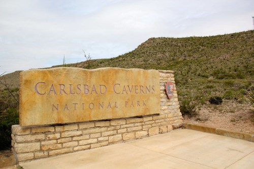Sign for Carlsbad Caverns National Park, set against a rocky landscape under a cloudy sky.