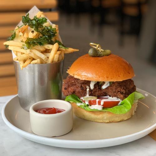 A crispy fried chicken sandwich with lettuce, tomato, and sauce, served with fries and a side of ketchup.