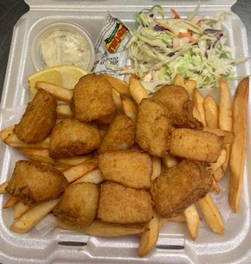 A takeout container filled with golden fried fish bites, French fries, coleslaw, and a side of dipping sauce.