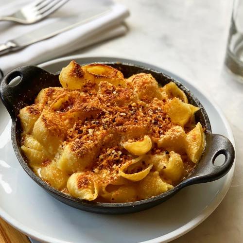 A cast-iron dish of baked macaroni and cheese topped with crispy breadcrumbs, served on a white plate.