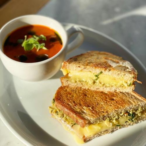 A grilled cheese sandwich with pesto, served with a cup of tomato soup garnished with herbs.