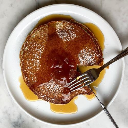 A stack of golden pancakes drizzled with syrup and topped with a dollop of jam, served on a white plate.
