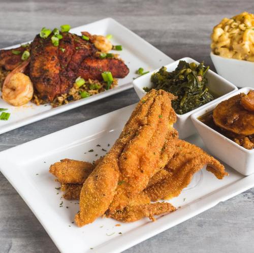 A plate of fried catfish with greens, macaroni, and a side of sweet plantains, alongside a dish of shrimp and chicken.