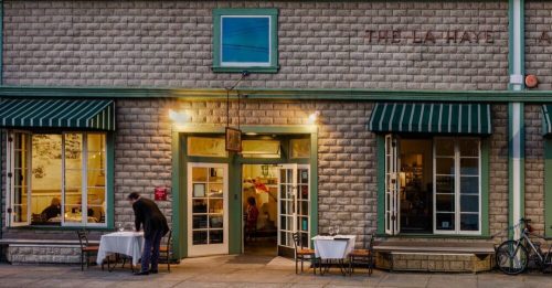 A cozy restaurant exterior with green awnings, tables outside, and a person entering through double doors.