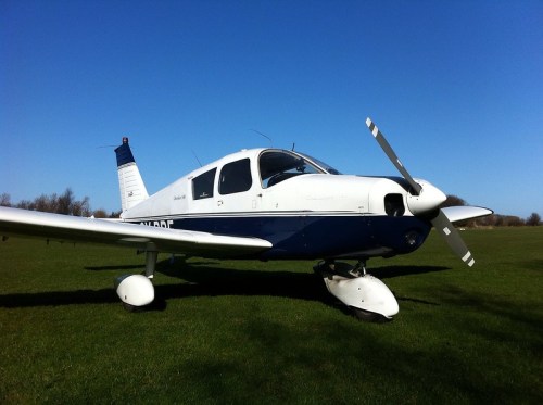A small white and blue airplane parked on a grassy field under a clear blue sky.