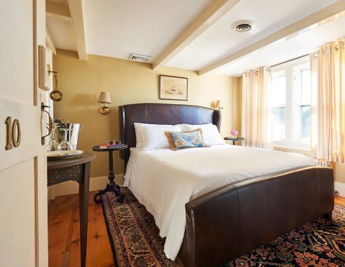 Cozy bedroom with a large bed, warm lighting, and a decorative rug, featuring a small table and window with curtains.