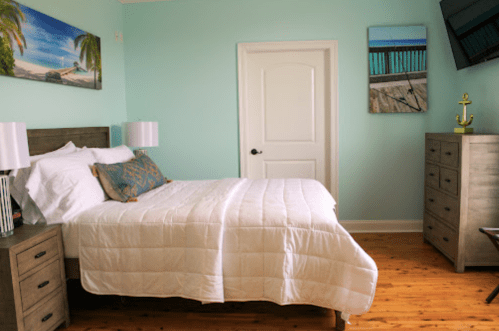 Cozy bedroom with a light blue wall, a queen bed, nightstands, and beach-themed decor.